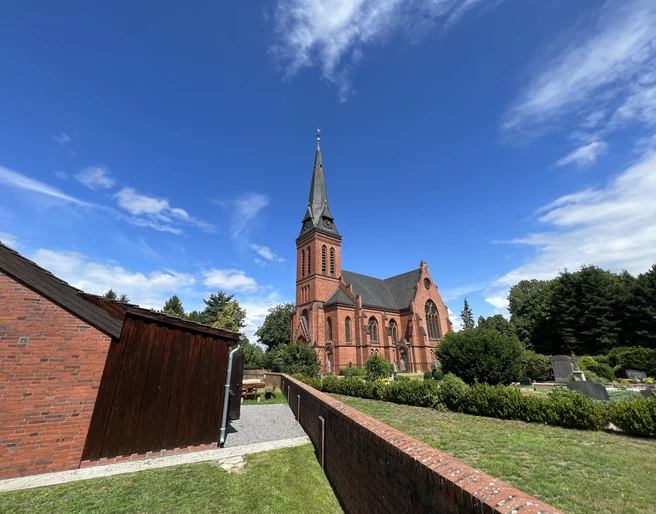 St. Jakobi-Kirche zu Wittlohe Die rote Backstein-St. Jakobi-Kirche in Wittlohe erhebt sich vor einem klaren blauen Himmel.
