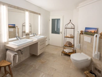 Badezimmer. Beige gefließtes Bad mit zwei großen Waschtischen, Unterschrank, Toilette und Regal