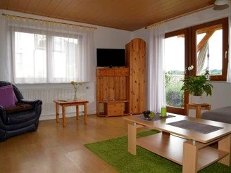 Vorne ein Couchtich, links einzelner Sessel, rechts ein Schrank mit Fernseher