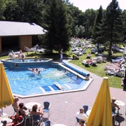 Roetgen Therme Außenpool Außenpool in sommerlichem Ambiente mit Personen auf Liegestühlen und Schwimmenden im Wasser, umgeben von Wiesen und Bäumen.