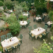 Blick auf die Gartenwirtschaft mit vielen Tischen, Stühlen, Blumen und frischen Kräutern