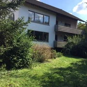 Außenansicht, weiße Hausfassade und zwei Balkone, davor Garten mit Büschen