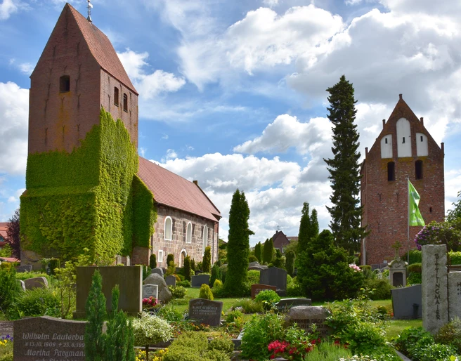 St-Johannes Kirche Die St.-Johannes-Kirche erhebt sich majestätisch über den gepflegten Kirchhof mit blühenden Beeten und Grabsteinen. Der Turm ist mit Efeu bewachsen, was ihm ein malerisches Aussehen verleiht.