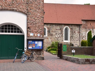 St-Johannes-Kirche Ziegelkirche mit rotem Dach, angeschlossenem Tor und Eingangsbereich; Fahrräder lehnen an der Wand.