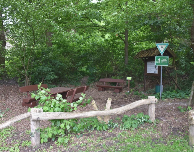 Bokeler Burg Im grünen Wald steht eine rustikale Holzgarnitur mit Tisch und Bänken nahe einem Weg; Schilder weisen auf Wanderstrecken hin.