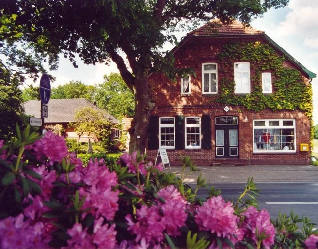 Tante Emma Laden Ein traditioneller Tante-Emma-Laden in einem Backsteinhaus, umgeben von blühendem Rhododendron.