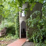 Kapelle "Unter den Linden" Eine kleine, runde Kapelle aus Stein, umgeben von Bäumen und grünem Laub.