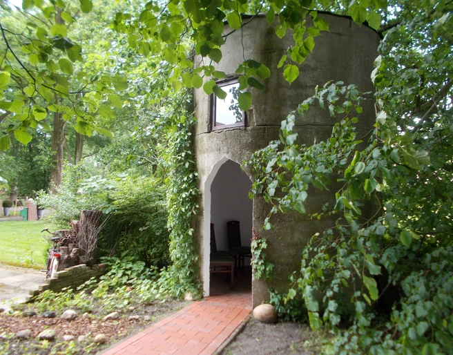 Kapelle "Unter den Linden" Eine kleine, runde Kapelle aus Stein, umgeben von Bäumen und grünem Laub.