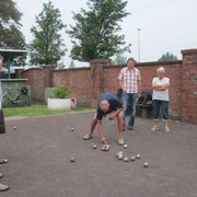 Donnerstag-Gruppe Eine Gruppe von Menschen spielt Boule auf einem Kiesplatz vor einer alten Backsteinmauer.