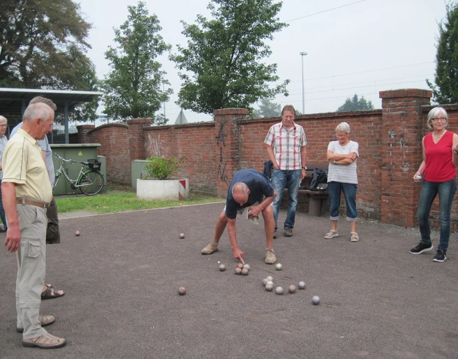 Donnerstag-Gruppe Eine Gruppe von Menschen spielt Boule auf einem Kiesplatz vor einer alten Backsteinmauer.
