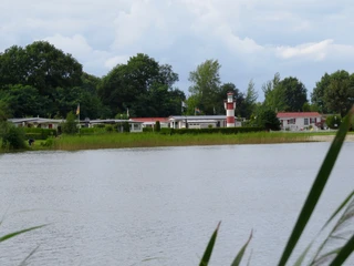 Ein idyllischer Campingplatz am See, umgeben von üppigem Grün und einem charakteristischen Leuchtturm.
