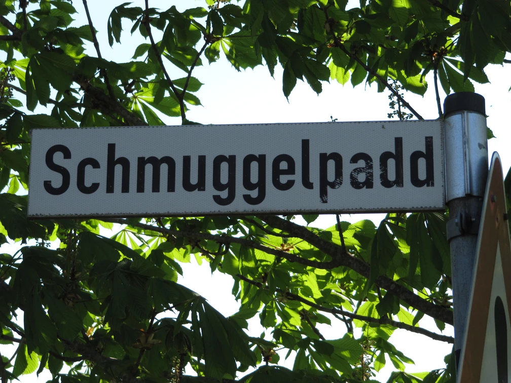 Wegweiser Schmuggelpadd Ein Straßenschild mit dem Namen "Schmuggelpadd", umgeben von grünen Kastanienblättern.