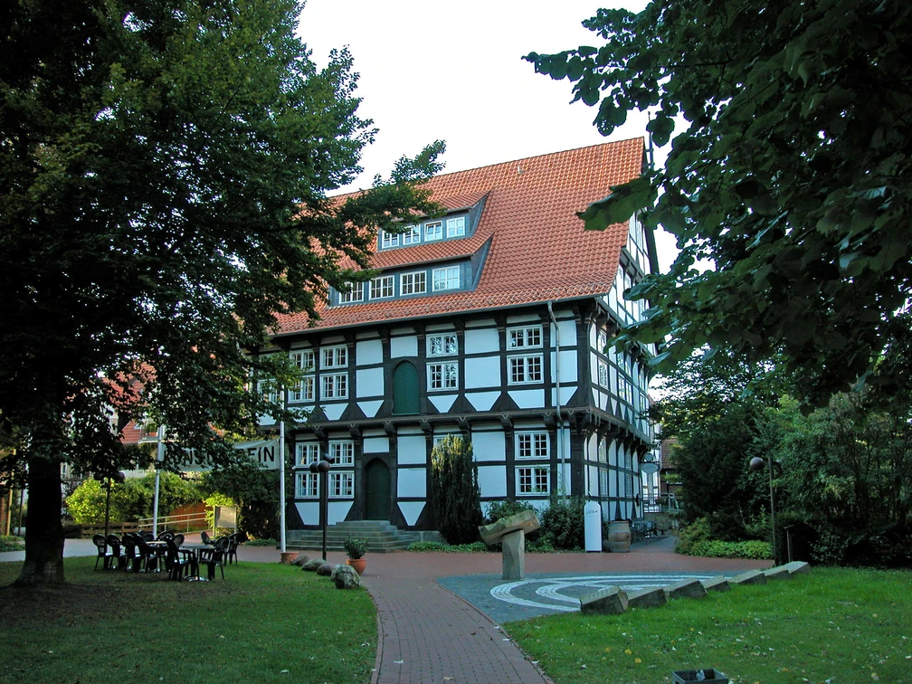 Abtei von außen Fachwerkgebäude mit rotem Ziegeldach, eingebettet zwischen großen, grünen Bäumen.