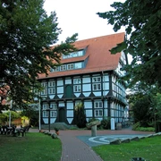 Abtei von außen Fachwerkgebäude mit rotem Ziegeldach, eingebettet zwischen großen, grünen Bäumen.