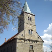 Petruskirche Steinhude Steinernes Kirchenschiff mit Kirchturm, schiefer Spitze und Uhr unter blauem Himmel mit Wolken.