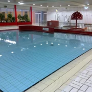 Wunstorf Elements Nichtschwimmerbecken Das Bild zeigt ein modernes Hallenbad mit einem nicht zu tiefen Beckenbereich. Die Fliesen haben eine helle, glänzende Oberfläche und sind in neutralen Tönen gehalten, was eine saubere und einladende Atmosphäre schafft. Pflanzen und Sitzgelegenheiten ergänzen das freundliche Ambiente.