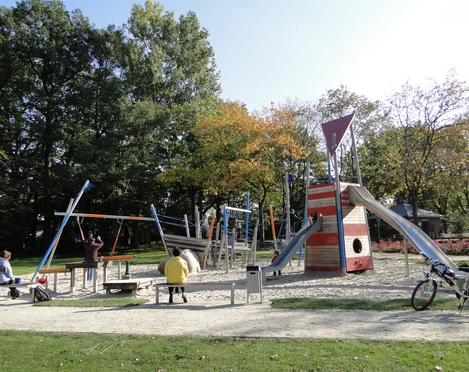 Spielgeräte auf dem Spielplatz im Park Verschiedene bunte und moderne Spielgeräte auf einem Sandspielplatz, umgeben von Grünflächen.