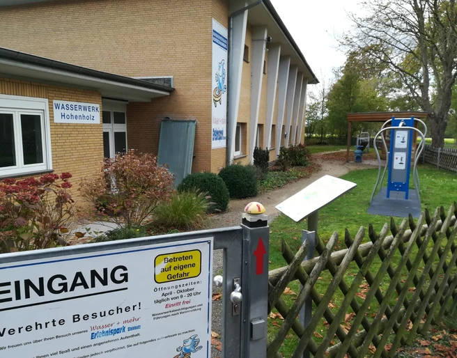 Wasser + mehr Erlebnispark Eingang Im Vordergrund ist der Eingang des Wasser + mehr Erlebnisparks in Hohenholz zu sehen. Ein Schild informiert über den Zugang.