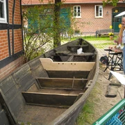 Restaurierung "Heske Deern" Das Bild zeigt ein altes, teilweise restauriertes Holzboot auf einem Platz vor einem Backsteingebäude.