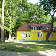 Ein gelbes Gebäude mit rotem Dach und mehreren Fenstern, eingebettet in einen grünen Park.