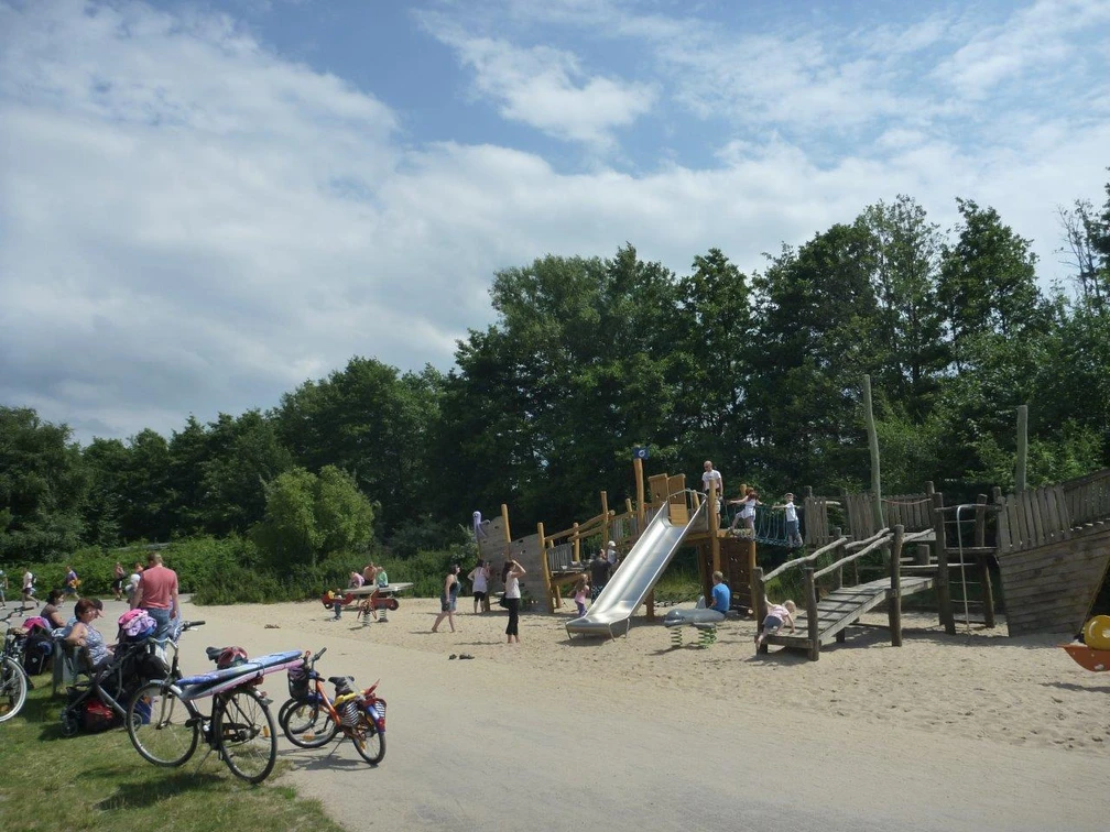 Ein lebendiger Spielplatz mit Holzkonstruktionen, Rutsche und Kindern beim Spielen im sonnigen Park.