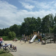 Ein lebendiger Spielplatz mit Holzkonstruktionen, Rutsche und Kindern beim Spielen im sonnigen Park.