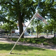 Treffpunkf für Gästeführungen Eine Fahne mit der Aufschrift "Treffpunkt Führungen" neigt sich neben einem Weg in einem grünen Parkbereich.