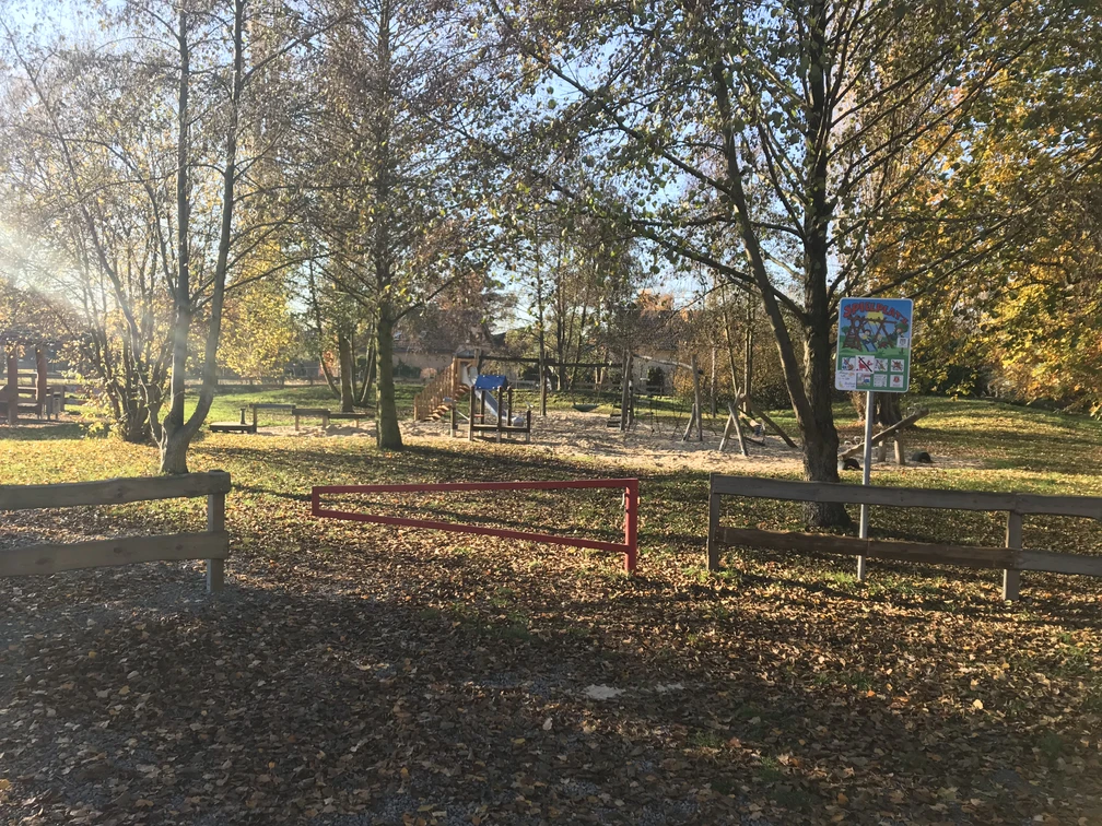 Spielplatz Försterwiese Spielplatz in herbstlicher Landschaft mit Schaukeln und Rutsche, umgeben von Bäumen und Grünfläche.