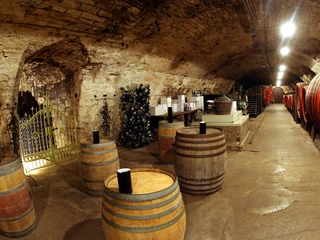 Sektkellerei Duprès  Ein rustikaler Weinkeller mit mehreren Holzfässern, einem geöffneten Tor und dekorativen Lichteffekten.