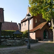 Grillplatz Aloys-Bunge-Platz Historischer Backsteinbau mit markantem Schornstein, überdachtem Sitzbereich und umgebenden Bäumen.
