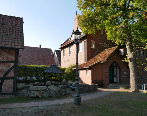 Grillplatz Aloys-Bunge-Platz Historischer Backsteinbau mit markantem Schornstein, überdachtem Sitzbereich und umgebenden Bäumen.