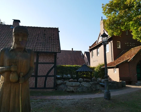 Grillplatz Aloys-Bunge-Platz Holzskulptur vor Fachwerkhäusern auf dem Aloys-Bunge-Platz, umgeben von Bäumen und einem Grillplatz.