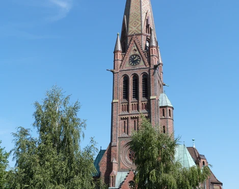 Kirche Hagenburg Front Backsteinkirche mit hohem, verzierten Turm und Uhr, umrahmt von Bäumen unter klarem Himmel.
