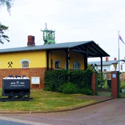 Das Bergbaumuseum Altenhagen zeigt ein gelbes Gebäude mit Förderturm und alten Förderwagen, umgeben von Bäumen.