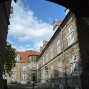 Schloss Landestrost Im Innenhof des Schlosses Landestrost bieten historische Backsteinfassaden und rote Dachziegeln eine beeindruckende Kulisse unter einem blauen Himmel mit weißen Wolken.