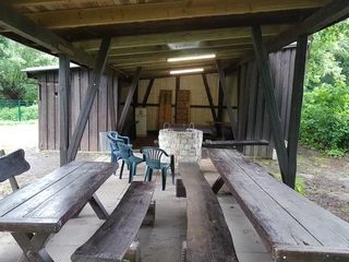 Grillhütte Hagenburg Grill Offener Unterstand mit Holztischen, Bänken und einem gemauerten Grill, teils umgeben von Bäumen.