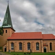 Kirche in Schwarmstedt Backsteinkirche in Schwarmstedt mit grünem Turm und rotem Dach. Umgeben von Bäumen und Wolken.