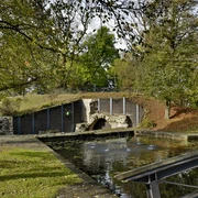 Neustadt Erichsberg Ein runder, von Bäumen gesäumter Teich vor einem alten Steinbogen in ruhiger naturnaher Umgebung.