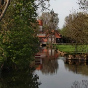 Ecksteinmühle  Historische Wassermühle am ruhigen Fluss, umgeben von grünen Bäumen und einem klaren Himmel.