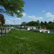 Schiffsanleger Höxter Grünes Ufer am Schiffsanleger Höxter mit Ausflugsboot, Spazierweg und blühenden Bäumen im Hintergrund.