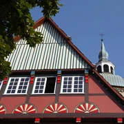 Historisches Fachwerkhaus in Wiedenbrück Fachwerkhaus mit bunten Ornamenten, im Hintergrund Kirchturm unter blauem Himmel sichtbar.