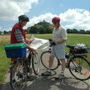 Der Desenberg: Wahrzeichen des Warburger Landes Zwei Radfahrer studieren eine Karte vor einem bewachsenen Hügel mit einer Ruine an der Spitze.