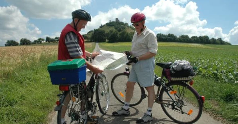 Der Desenberg: Wahrzeichen des Warburger Landes Zwei Radfahrer studieren eine Karte vor einem bewachsenen Hügel mit einer Ruine an der Spitze.