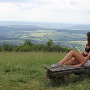 Ausblick vom Köterberg Zwei Personen sitzen auf einer Bank und blicken über eine weitläufige, grüne Hügellandschaft.