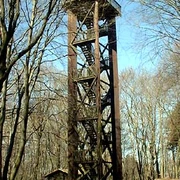 Hölzerner Aussichtsturm im Wald mit freiem Blick durch die Bäume auf den blauen Himmel.