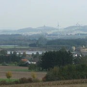 Blick zu den Kiesteichen Blick auf Kiesteiche mit umliegenden Feldern, Windrädern und sanften Hügeln im Hintergrund.