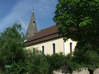 Kirche Stapelage Die Kirche Stapelage mit spitzem Turm, umgeben von Bäumen und strahlend im Sonnenlicht.