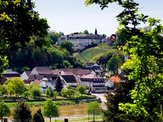 Abtei-vom-heiligen-kreuz-beverungen-herstelle-F-Grawe.jpg Blick auf die Abtei vom Heiligen Kreuz in Herstelle, umgeben von dichten Wäldern und einem Fluss.