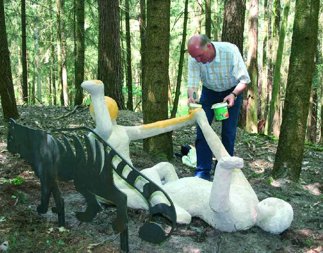 Wilhelm Wortberg Ein Mann bemalt eine liegende Skulptur im Wald, daneben steht eine Metallfigur mit Streifen.