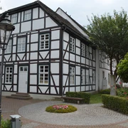 Haus des Gastes Fachwerkhaus mit weißen Wänden und dunklen Holzbalken, umgeben von gepflegten Grünanlagen.